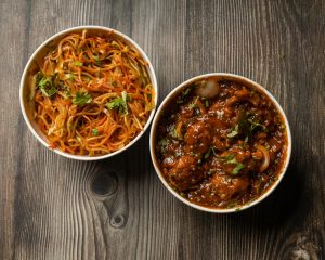 Vibrant bowls of Indo-Chinese noodles and Manchurian on a rustic wooden surface.